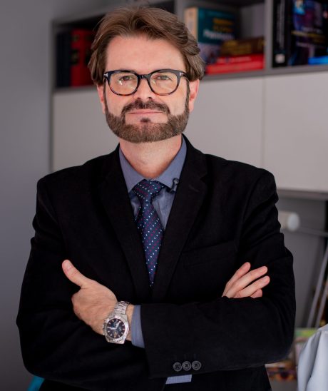 Retrato profissional do Dr. Fábio Lopes, cirurgião de cabeça e pescoço, de braços cruzados em seu consultório.